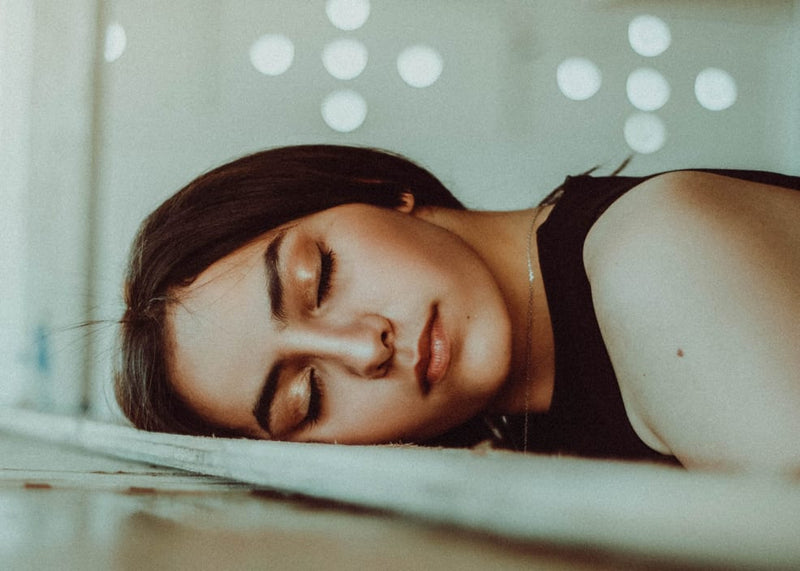 Woman lying down with eyes closed, blurred lights in the background