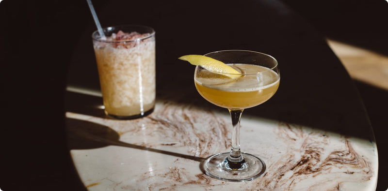 Two cocktails on a marble surface with a dark background