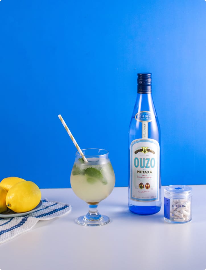 Bottle of Metaxa Ouzo with a glass of lemonade and lemons on a blue background