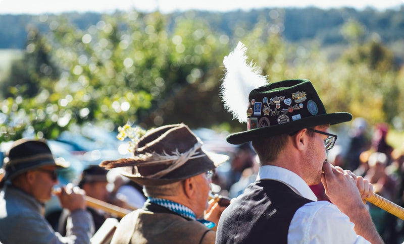 People in traditional Bavarian clothing with hats and feathers outdoors.