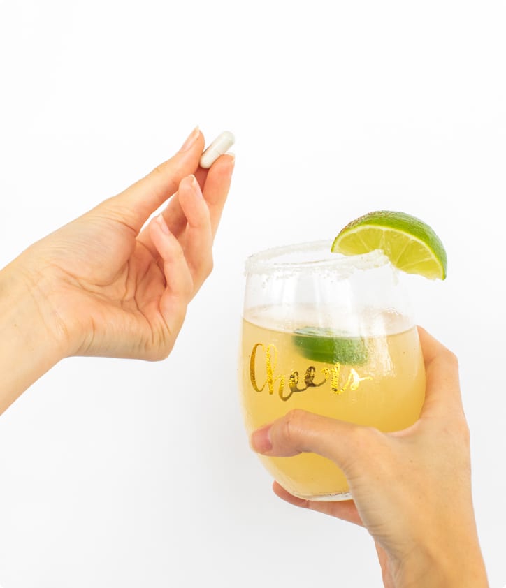 Hand holding a glass of yellow drink with a lime wedge on a white background