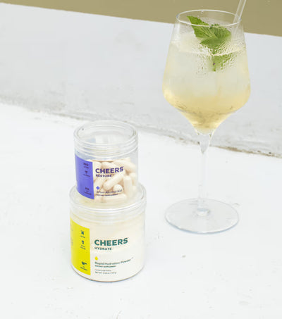 Jar of 'Cheers' protein powder next to a glass of a light-colored beverage with mint leaves on a white surface.