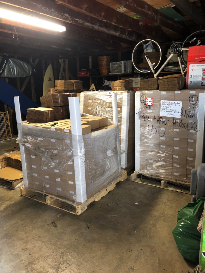 Pallets of boxes in a warehouse setting with various items in the background.